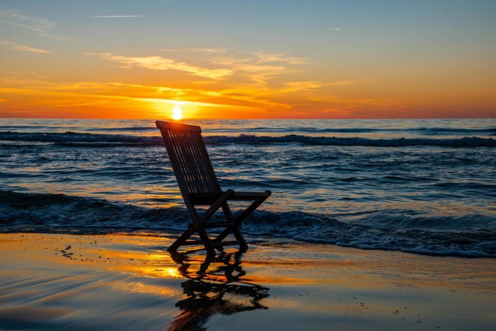 Tranquil sunset at the beach with waves and a chair reflecting in the ocean.